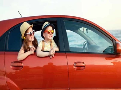 Children in sunglasses looking out of red car